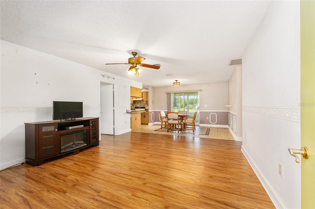 A living room with wood-look flooring, a television console, and an adjacent dining area — 7360 SW 15TH PLACE, OCALA, FL