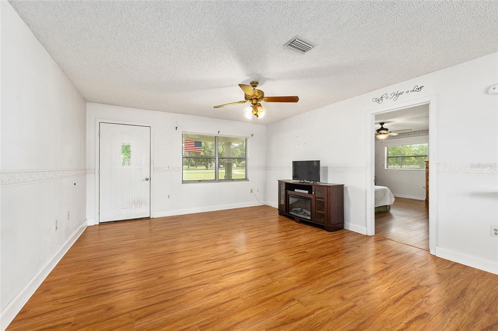 A living room with wood-look flooring, a ceiling fan, and a doorway leading to another room — 7360 SW 15TH PLACE, OCALA, FL