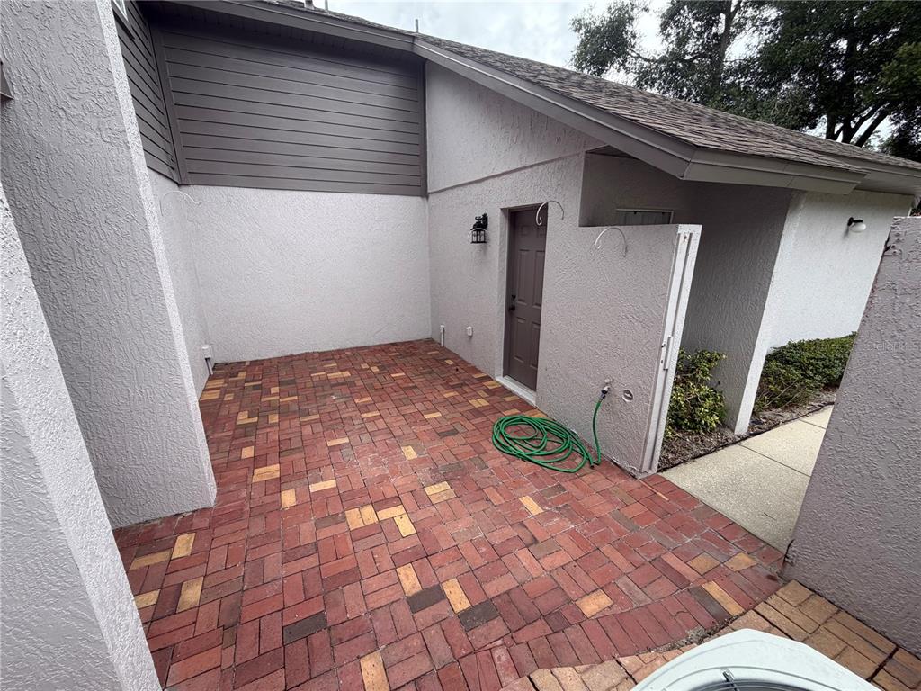 A brick-paved patio area features a brown door, a green garden hose, and stucco walls — 110 OLIVE TREE CIRCLE UNIT 110, ALTAMONTE SPRINGS, FL