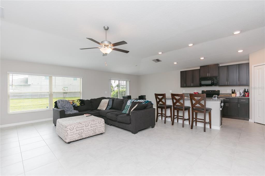 An open-concept living room and kitchen featuring a gray sectional, ottoman, and dark cabinetry — 13608 WILLOW BLUESTAR LOOP, RIVERVIEW, FL
