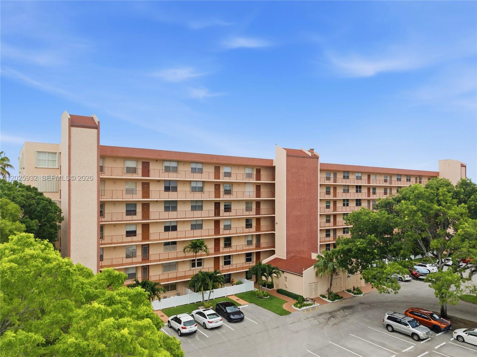 An exterior view of a multi-story apartment building with a parking lot and trees — 14623 Bonaire Blvd # 405, Delray Beach FL 33446, DELRAY BEACH, FL