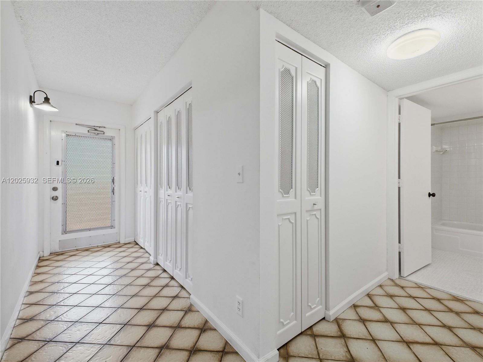 A hallway with white louvered closet doors, tiled floors, and a view into a bathroom — 14623 Bonaire Blvd # 405, Delray Beach FL 33446, DELRAY BEACH, FL