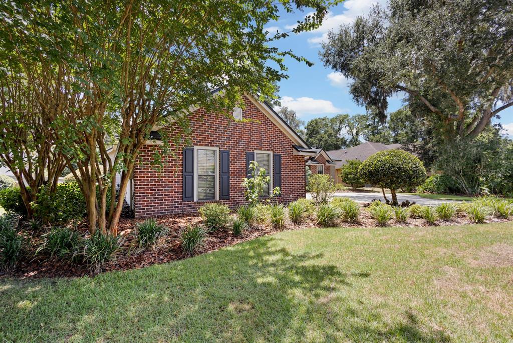A brick house with dark shutters is surrounded by trees and a landscaped front yard — 13573 NW 8TH ROAD, NEWBERRY, FL