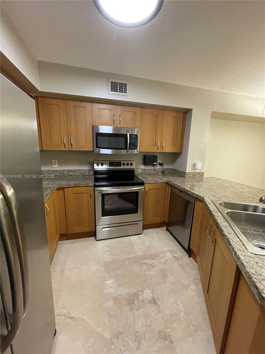 A kitchen features light wood cabinets, granite countertops, stainless steel appliances, and tile flooring — 3153 Clint Moore Rd # 106, Boca Raton FL 33496, BOCA RATON, FL