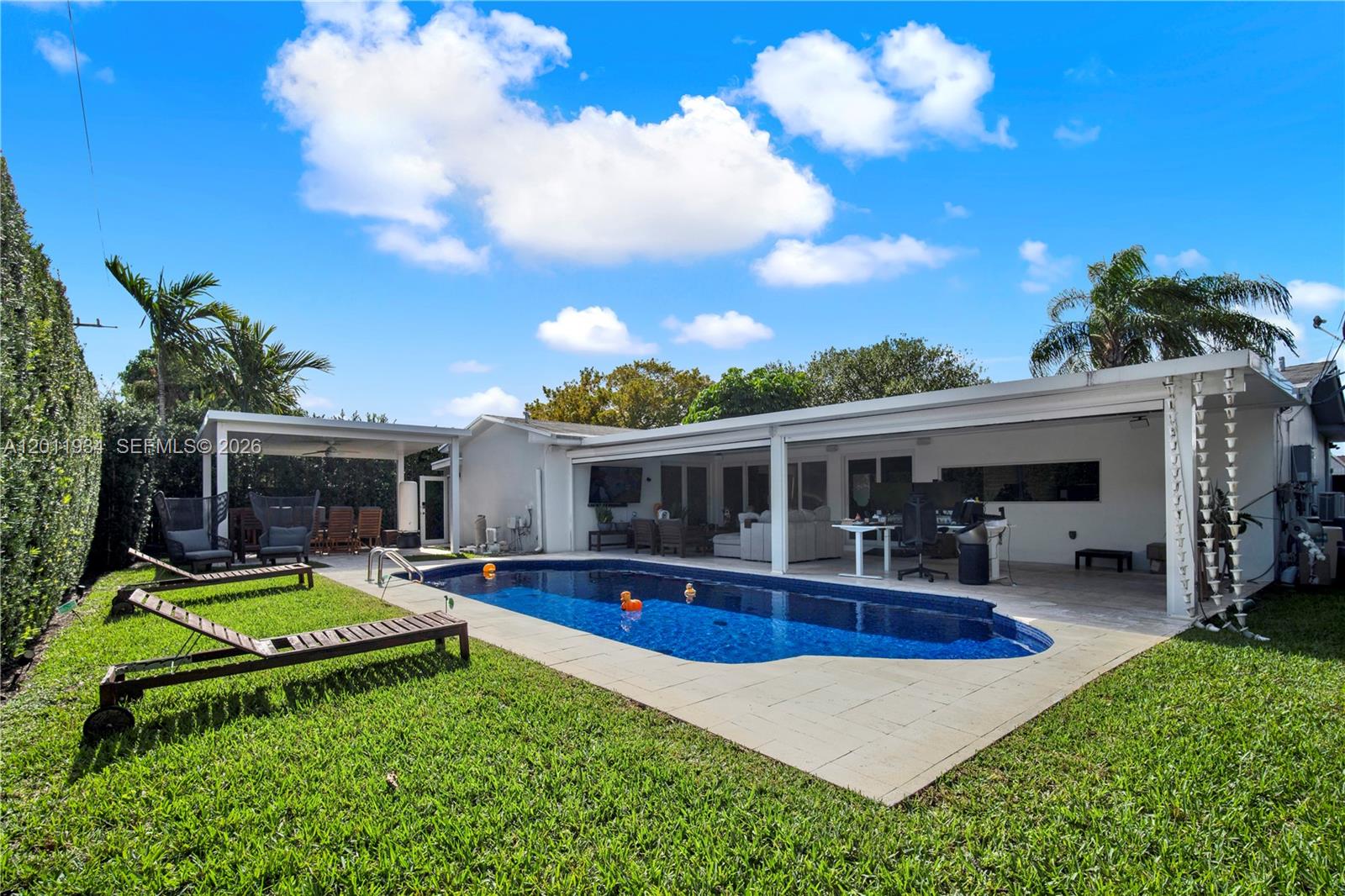 A backyard features a swimming pool, a covered patio, and lounge chairs on the grass — 21015 NE 19th Ct, Miami FL 33179, MIAMI, FL