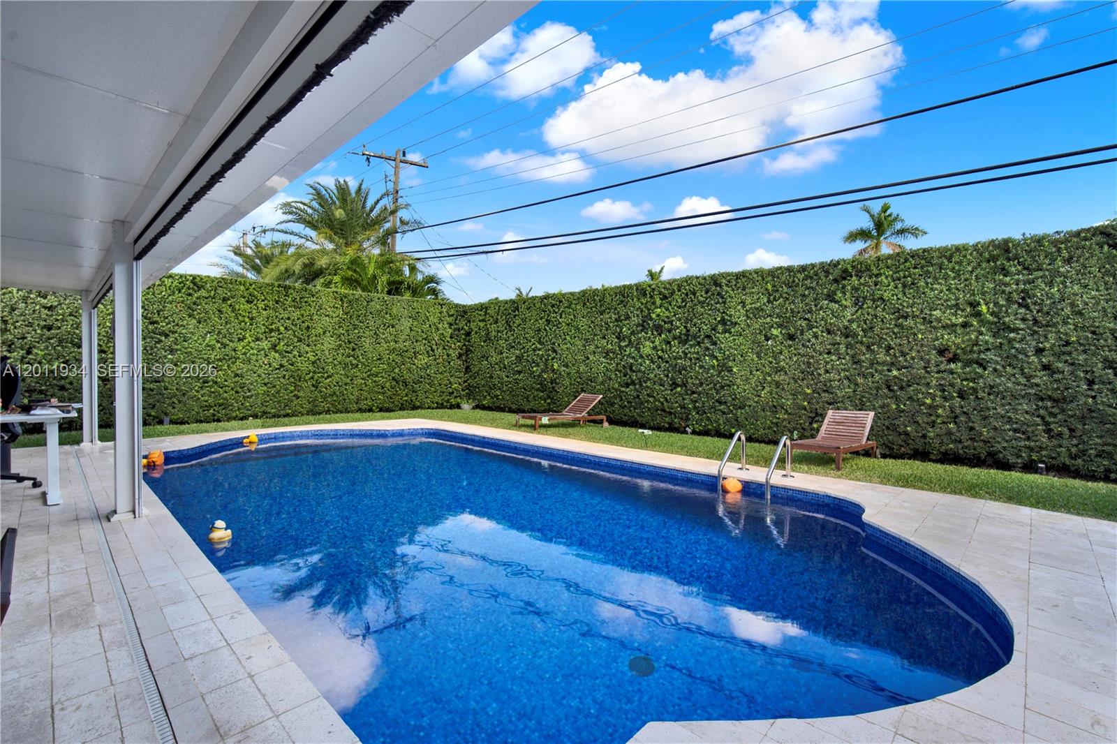 A backyard swimming pool features a tiled deck and a tall privacy hedge — 21015 NE 19th Ct, Miami FL 33179, MIAMI, FL