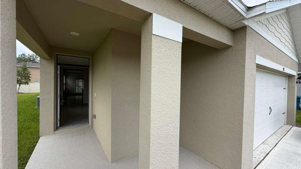 A beige stucco home exterior features a covered entryway and a white garage door — 1511 CATBRIAR WAY, DAVENPORT, FL