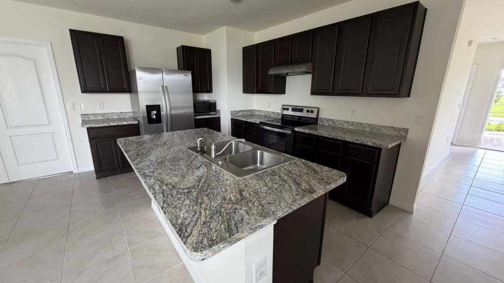 A kitchen features dark wood cabinets, granite countertops, a center island, and stainless steel appliances — 1511 CATBRIAR WAY, DAVENPORT, FL