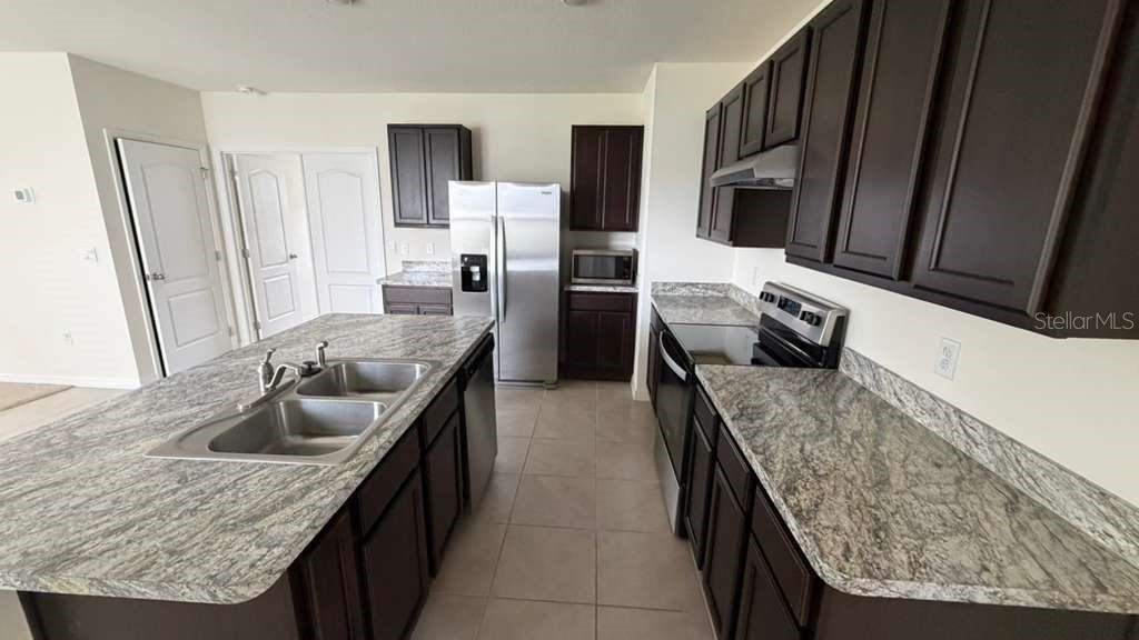 A kitchen features dark wood cabinets, granite countertops, a center island, and stainless steel appliances — 1511 CATBRIAR WAY, DAVENPORT, FL