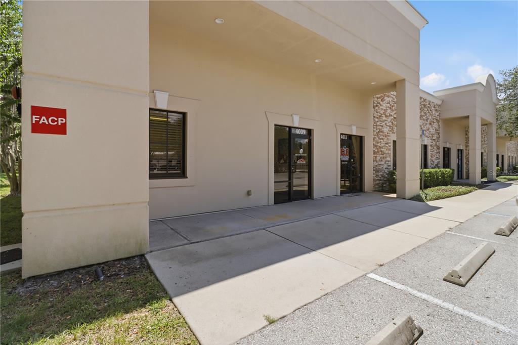 The exterior of a commercial building features a covered walkway, tan stucco walls, and glass doors — 4009 W 1ST STREET, SANFORD, FL
