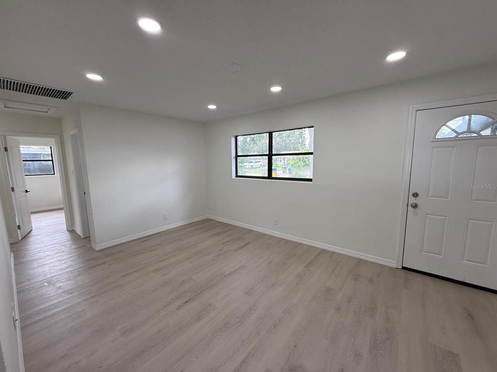 A bright, empty room features light wood-look flooring, recessed lighting, and a white front door — 430 LUCILLE STREET, BARTOW, FL