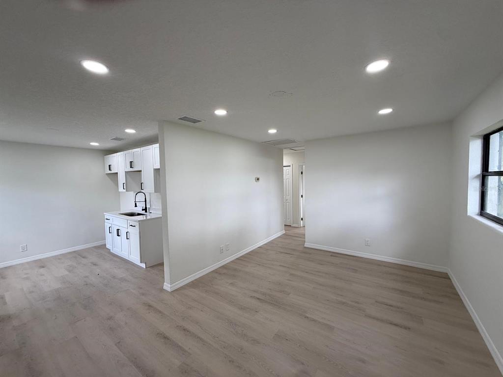 A kitchen with white cabinets and a sink opens into a living area with light flooring — 430 LUCILLE STREET, BARTOW, FL