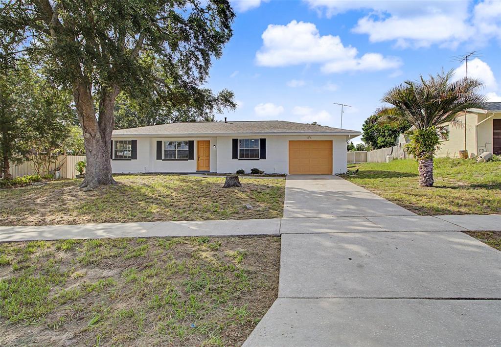 A white single-story house with a tan garage door and a large tree in front — 12368 MAYBERRY ROAD, SPRING HILL, FL