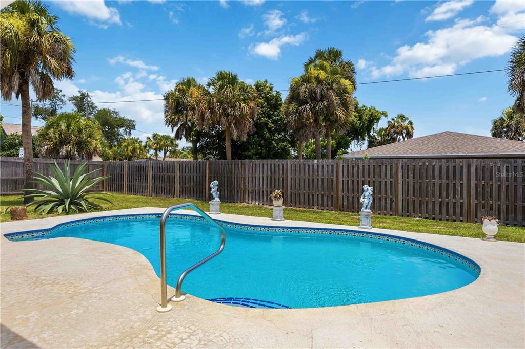 A backyard swimming pool with a metal handrail sits in front of a wooden fence — 440 LYCHEE ROAD, NOKOMIS, FL