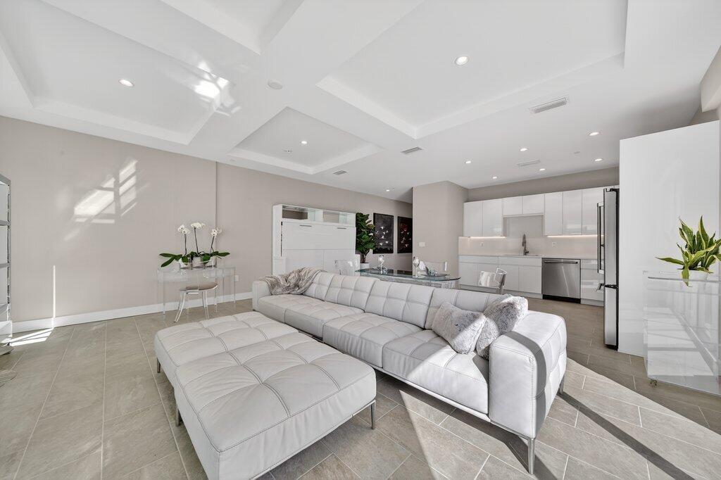 A modern open-concept living room features a white tufted sofa, ottoman, and a sleek kitchen — 41 SW Seminole Street # 209, Stuart FL 34994, STUART, FL