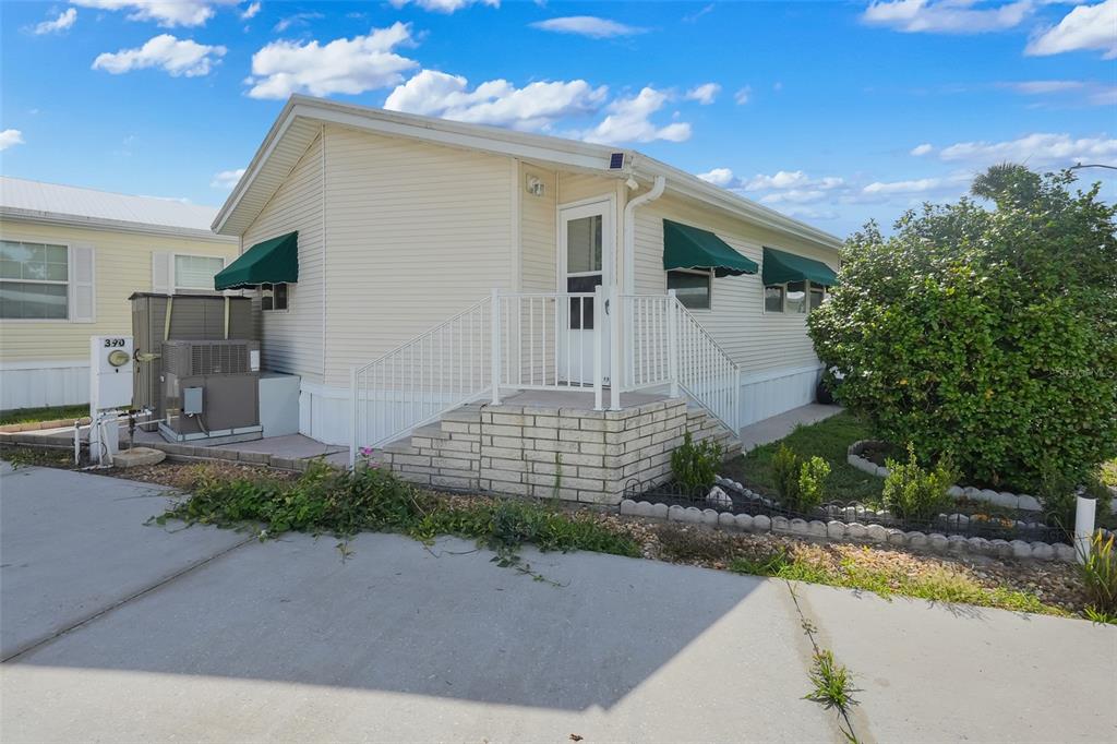 A light-colored manufactured home features a white staircase, green window awnings, and a concrete driveway — 9000 US HIGHWAY 192 UNIT 389, CLERMONT, FL