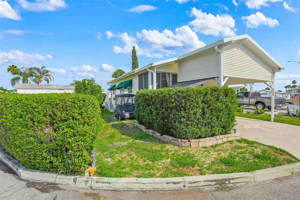 A mobile home with a carport, a golf cart, and a large hedge in front — 9000 US HIGHWAY 192 UNIT 389, CLERMONT, FL