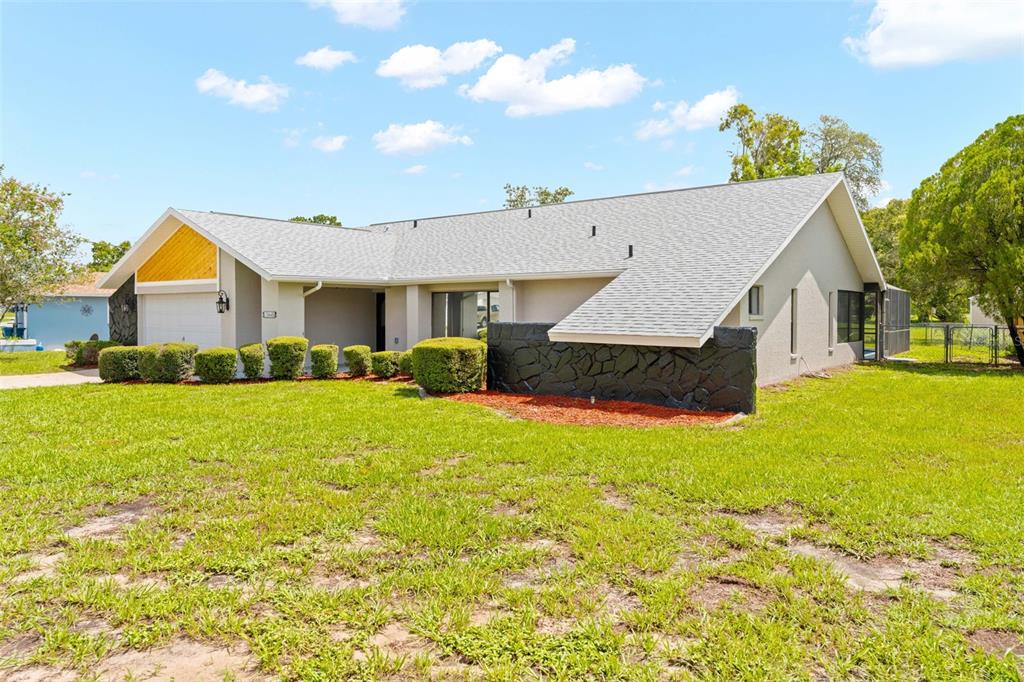 A single-story house with a light-colored exterior, a stone accent wall, and a garage — 13445 BANNER ROAD, SPRING HILL, FL