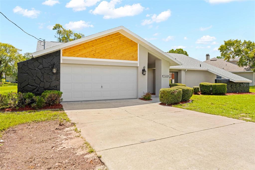 A single-story house features a white garage, wood-paneled gable, and black stone accent walls — 13445 BANNER ROAD, SPRING HILL, FL