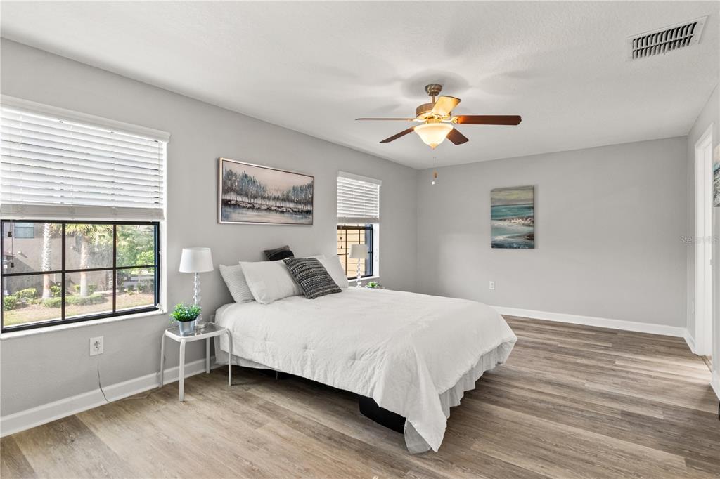 A bedroom features light gray walls, wood-look flooring, a white bed, and a ceiling fan — 3281 GENTLE DELL, WESLEY CHAPEL, FL