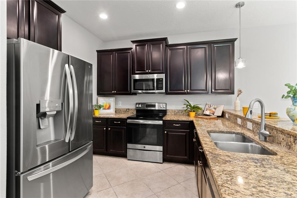 A kitchen features dark wood cabinets, granite countertops, stainless steel appliances, and tile flooring — 3281 GENTLE DELL, WESLEY CHAPEL, FL