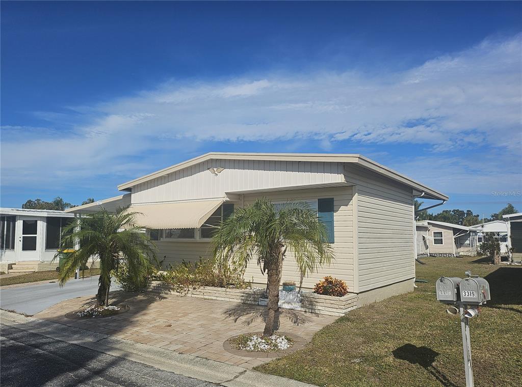 A single-story manufactured home with beige siding, a paved front patio, and two palm trees — 3317 OVERCUP OAK TERRACE, SARASOTA, FL