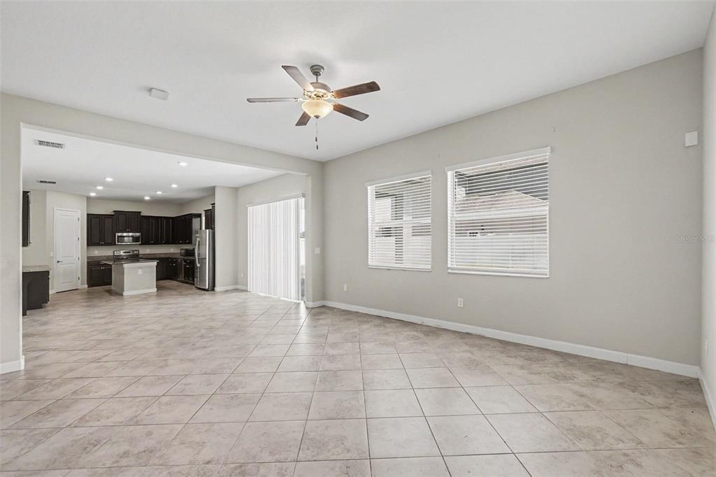 A spacious living area with tile flooring opens into a kitchen with dark cabinetry — 11701 NAVAJO SANDSTONE STREET, RIVERVIEW, FL