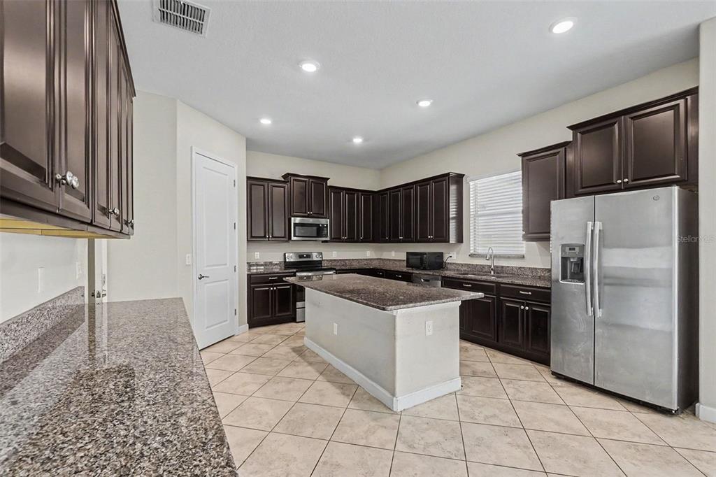 A kitchen features dark wood cabinets, granite countertops, a center island, and stainless steel appliances — 11701 NAVAJO SANDSTONE STREET, RIVERVIEW, FL