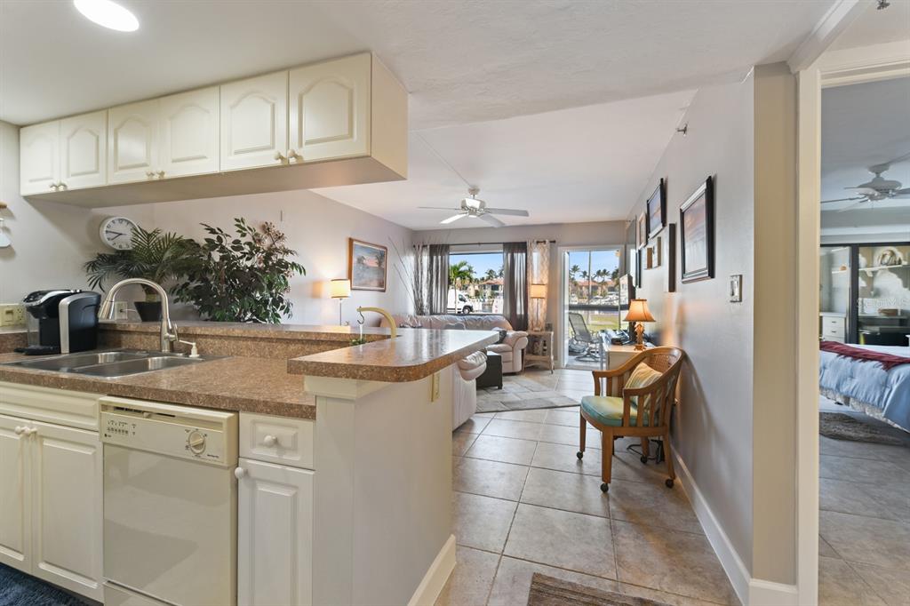 A kitchen with a breakfast bar overlooks a living room with a view of palm trees — 3170 MATECUMBE KEY ROAD UNIT 112, PUNTA GORDA, FL