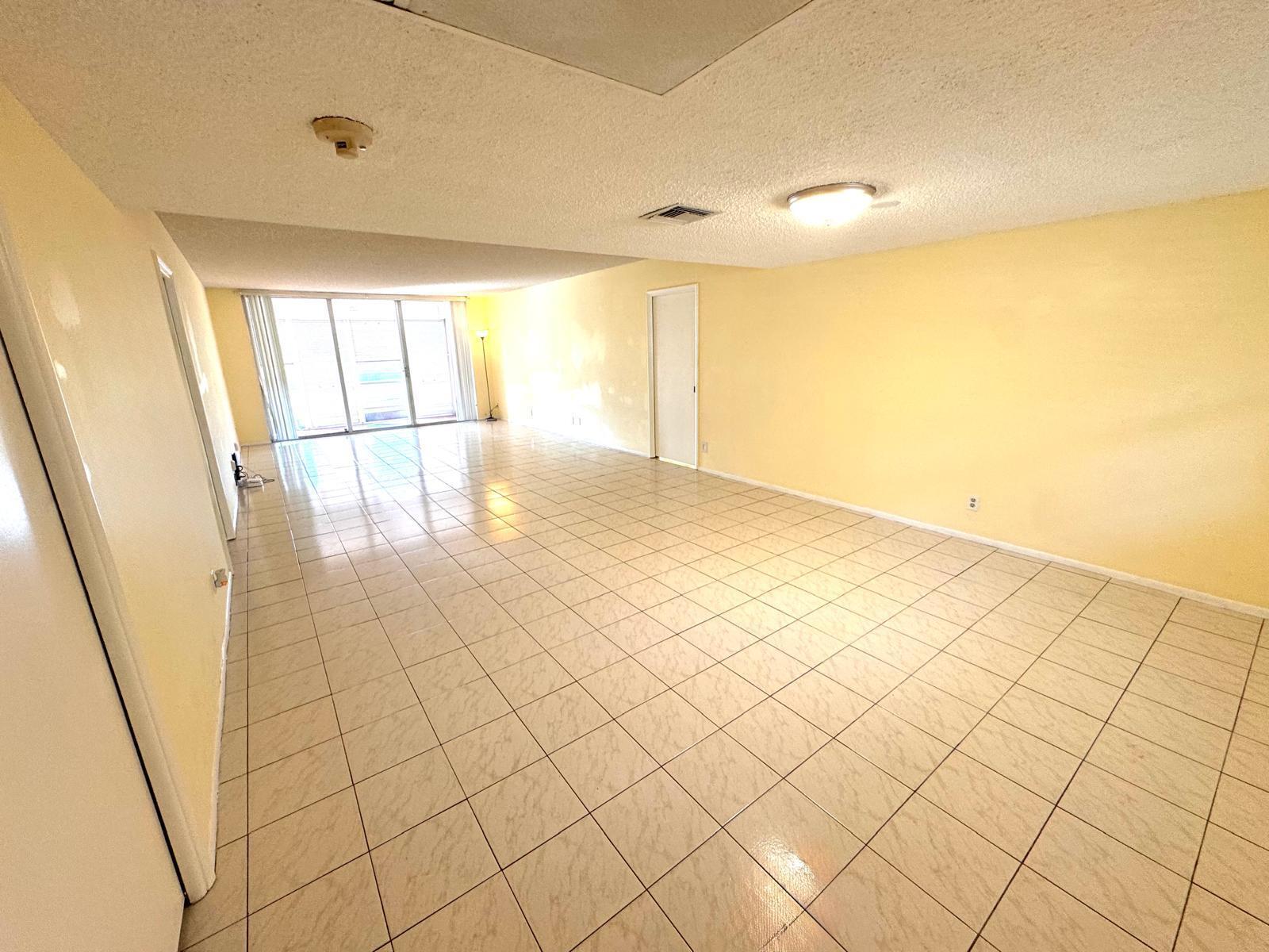 An empty room with light yellow walls, tiled flooring, and a sliding glass door — 901 Cypress Terrace # 103, Pompano Beach FL 33069, POMPANO BEACH, FL