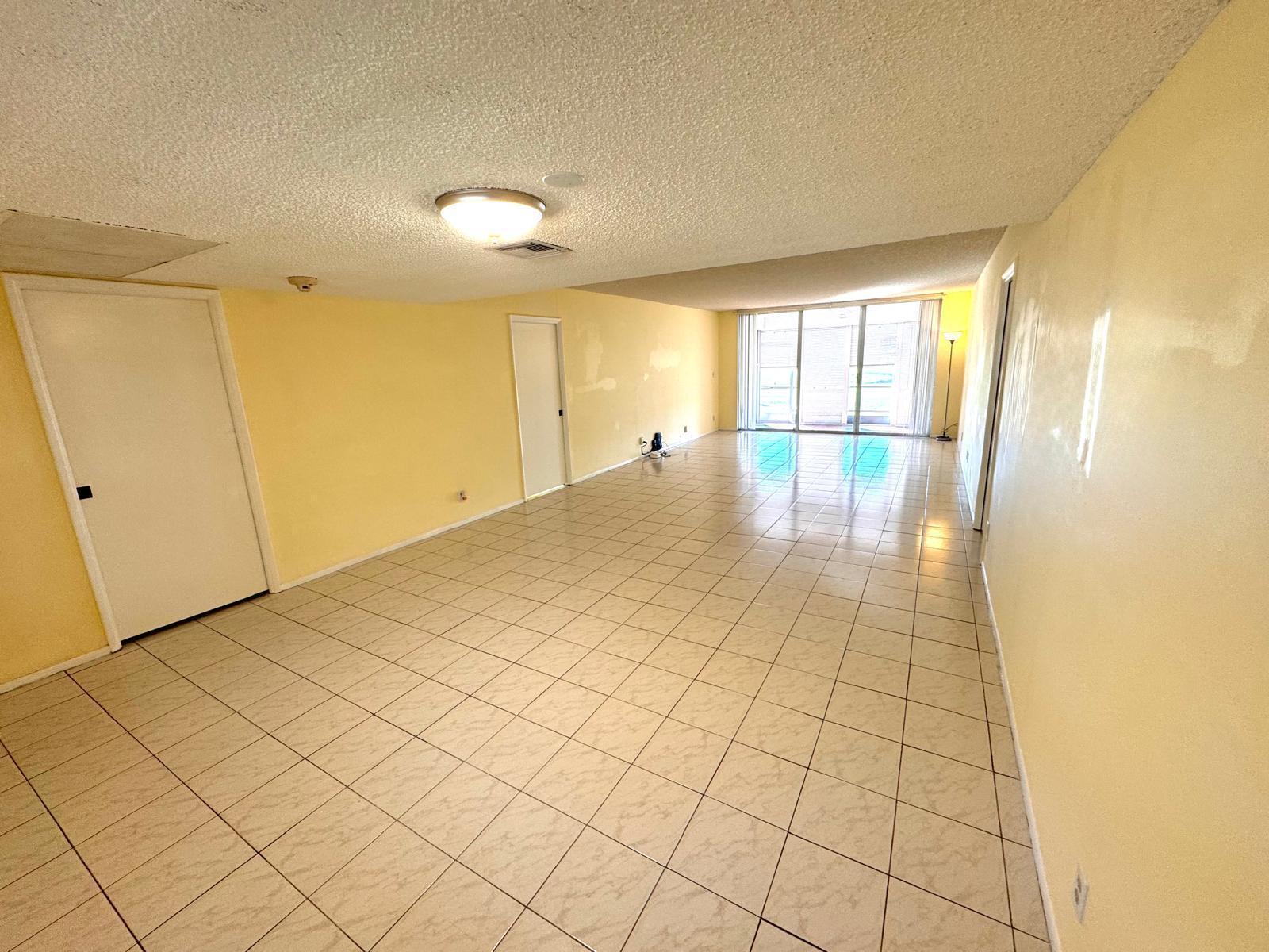 An empty room with yellow walls, tile flooring, a ceiling light, and sliding glass doors — 901 Cypress Terrace # 103, Pompano Beach FL 33069, POMPANO BEACH, FL