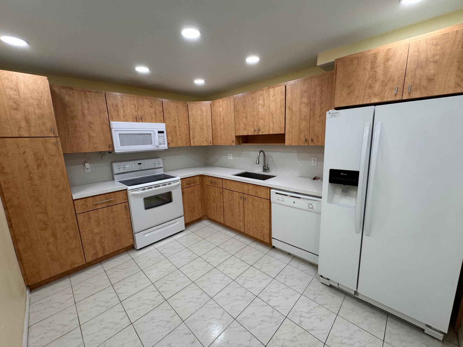 A kitchen features wood cabinets, white appliances, light countertops, and tiled flooring — 901 Cypress Terrace # 103, Pompano Beach FL 33069, POMPANO BEACH, FL