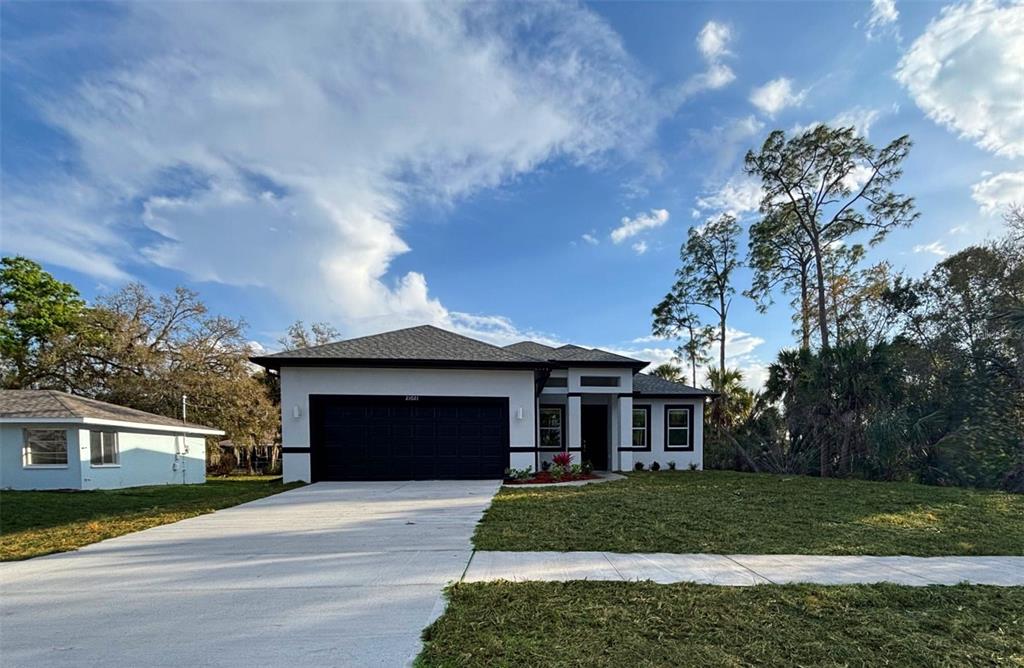 A modern single-story house with a black garage door and white exterior walls — 21021 PEACHLAND BOULEVARD, PORT CHARLOTTE, FL