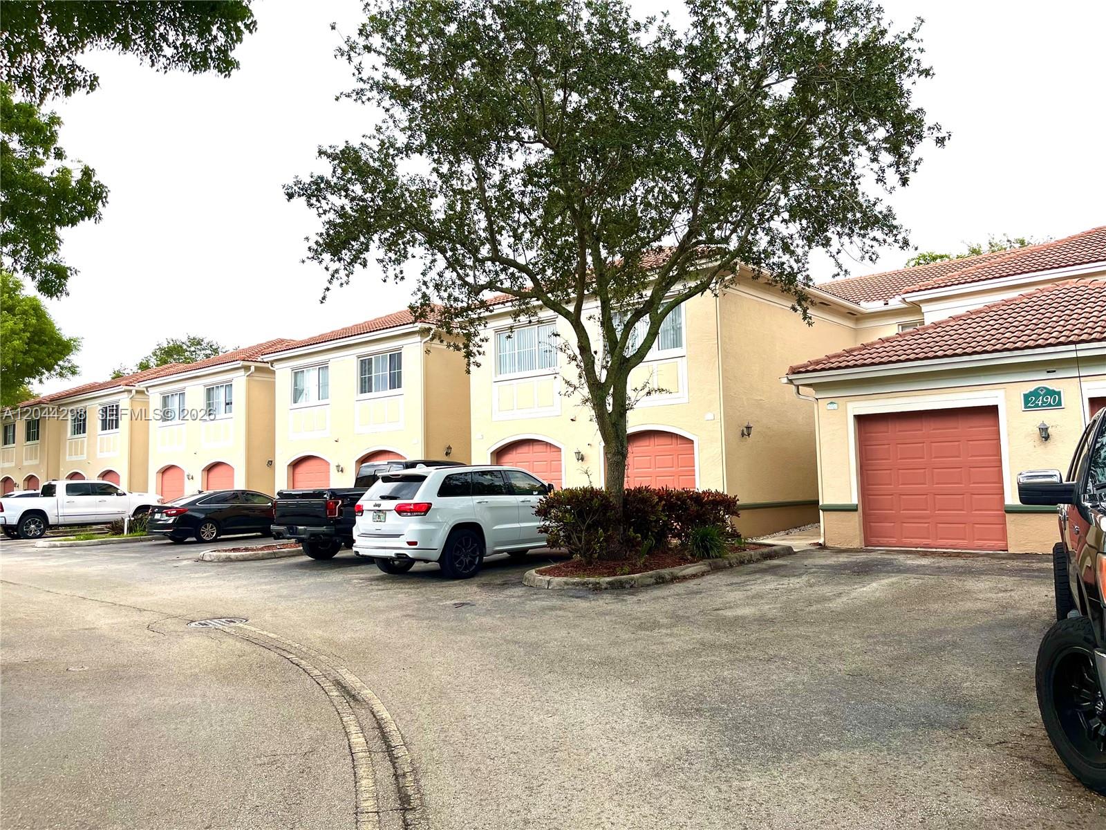 A row of two-story townhouses with tan stucco walls, red tile roofs, and garage doors — 2490 Centergate Dr # 207, Miramar FL 33025, MIRAMAR, FL