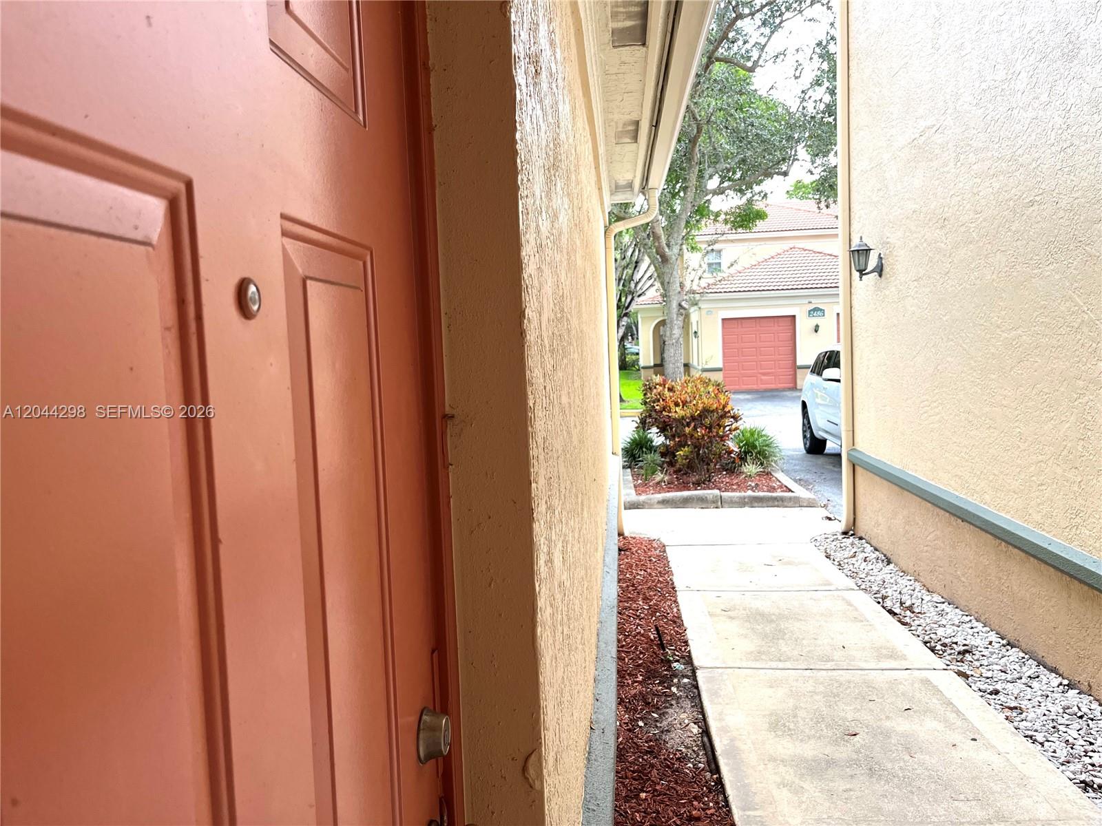 A view from a doorway looking out at a sidewalk, landscaping, and a neighboring house — 2490 Centergate Dr # 207, Miramar FL 33025, MIRAMAR, FL