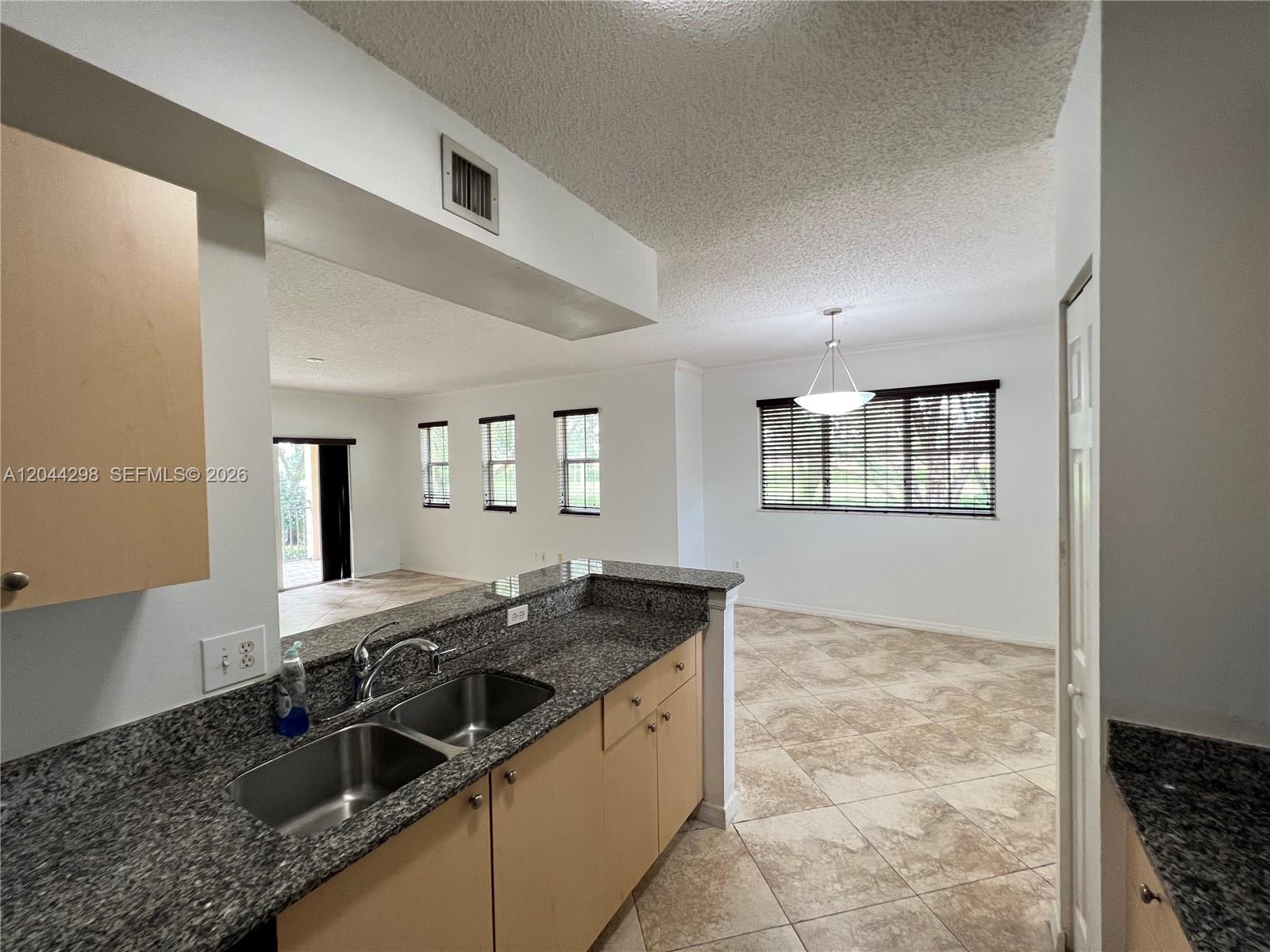 A kitchen with granite countertops and light wood cabinets overlooks a tiled dining area — 2490 Centergate Dr # 207, Miramar FL 33025, MIRAMAR, FL