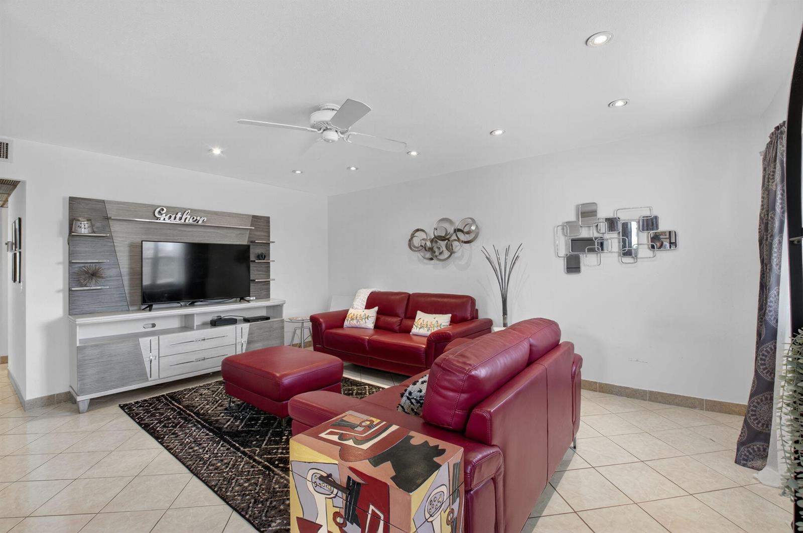 A living room features red leather sofas, a television console, and tiled flooring — 360 Seville # O, Delray Beach FL 33446, DELRAY BEACH, FL