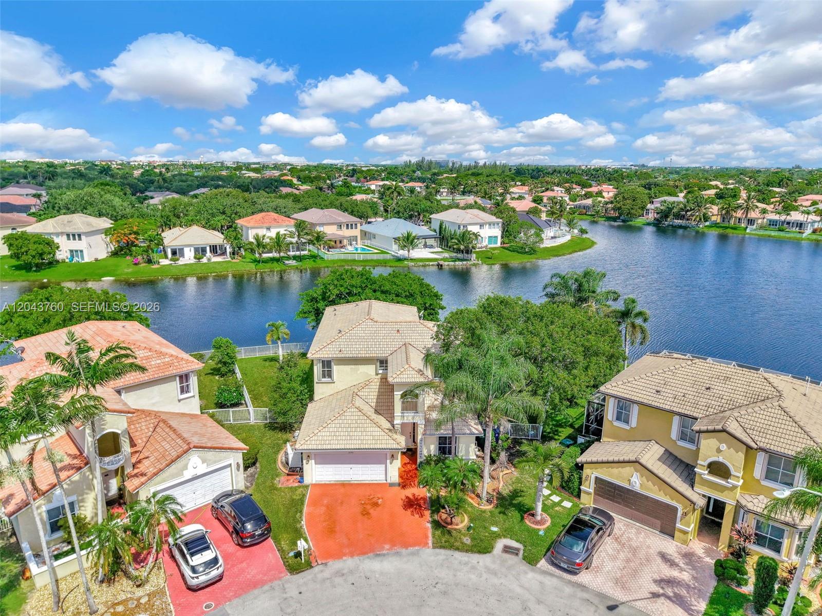 An aerial view shows three suburban houses with tile roofs situated along a lake — 13193 SW 30th St, Miramar FL 33027, MIRAMAR, FL