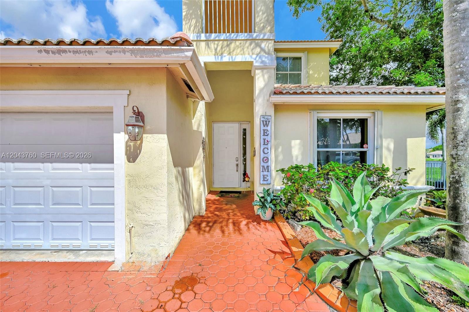 The exterior of a house features a white garage, a tiled walkway, and a welcome sign — 13193 SW 30th St, Miramar FL 33027, MIRAMAR, FL