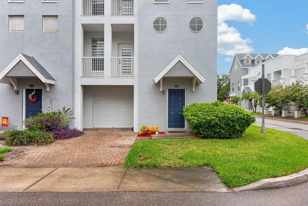 A gray multi-story townhouse with two blue front doors, a garage, and a small lawn — 4546 BAY SPRING COURT, TAMPA, FL