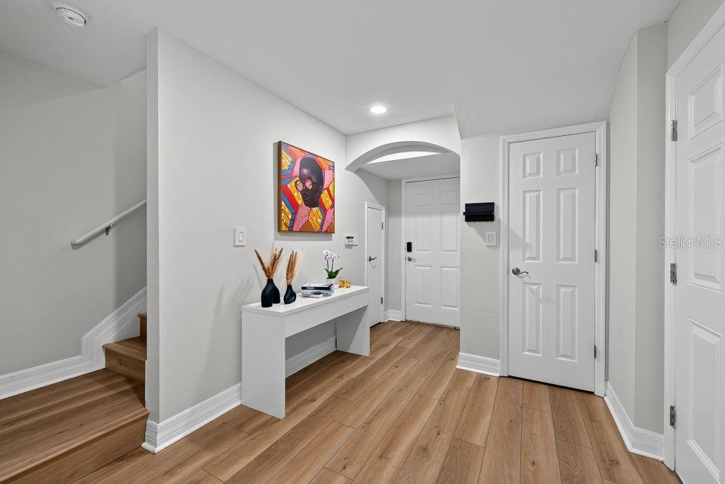 An entryway features light wood flooring, a white console table, wall art, and a staircase — 4546 BAY SPRING COURT, TAMPA, FL