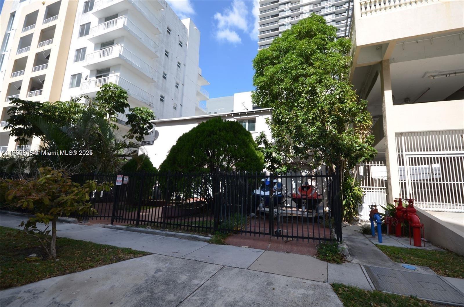 A fenced-in yard with trees and a jet ski sits between two multi-story buildings — 437 NE 30th St, Miami FL 33137, MIAMI, FL