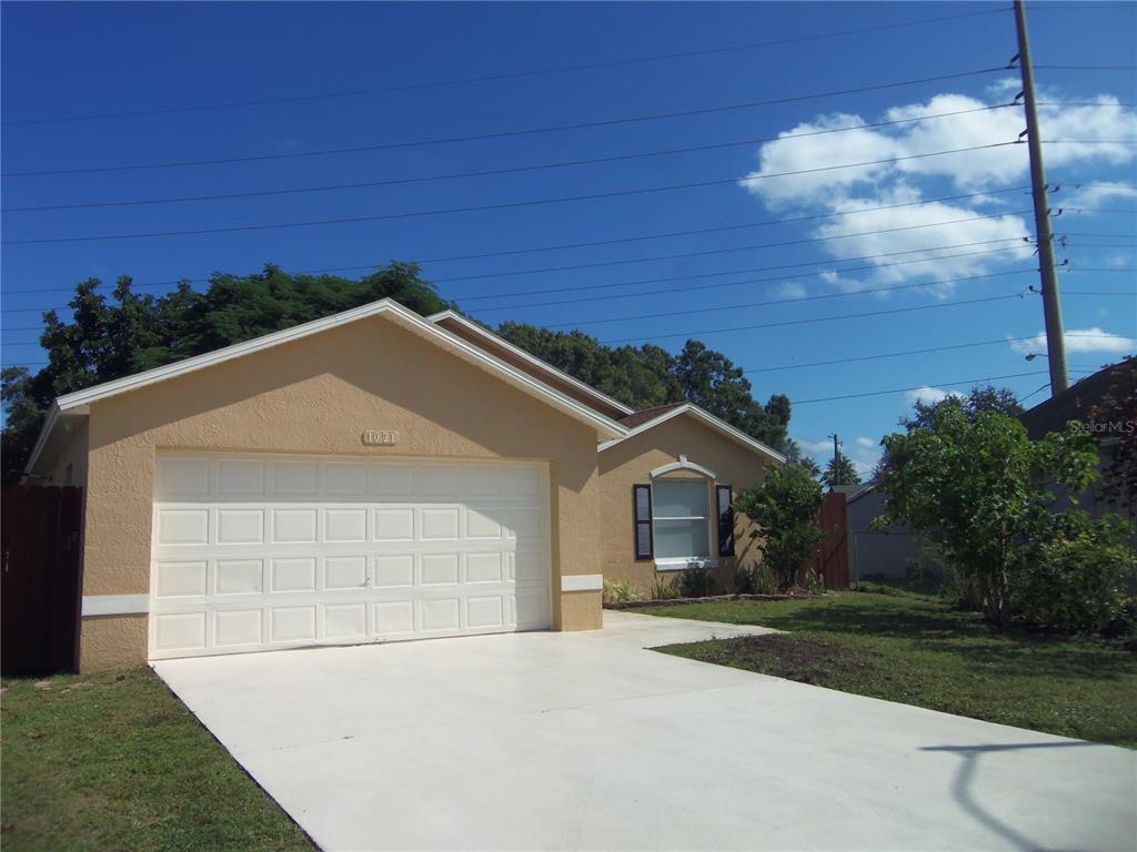 A single-story house with a tan stucco exterior, a white garage door, and a concrete driveway — 1021 GOLFSIDE COURT, KISSIMMEE, FL