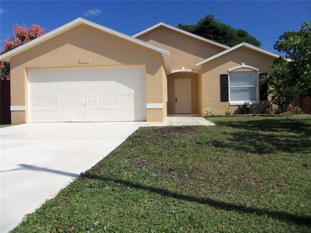 A single-story house with a tan stucco exterior, a two-car garage, and a front lawn — 1021 GOLFSIDE COURT, KISSIMMEE, FL