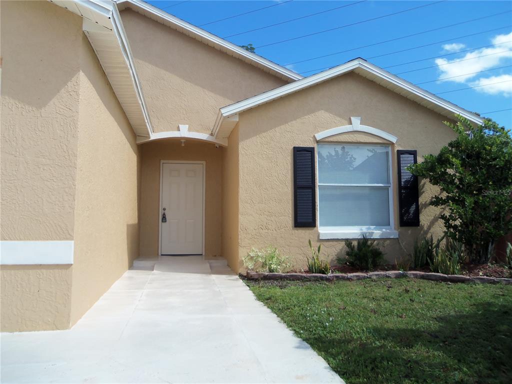 The exterior of a beige house features a white front door and a single window — 1021 GOLFSIDE COURT, KISSIMMEE, FL