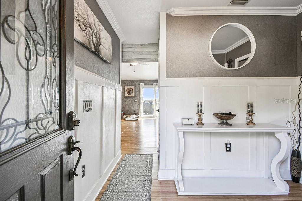 An entryway features white wainscoting, a console table, a round mirror, and a wood door — 6408 RUNNING BEAR DRIVE, LAKELAND, FL