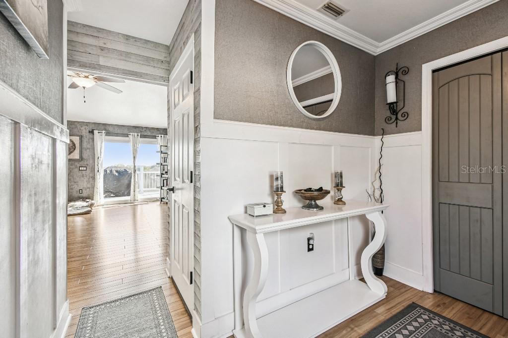 A hallway features white wainscoting, a console table, a round mirror, and wood-look flooring — 6408 RUNNING BEAR DRIVE, LAKELAND, FL