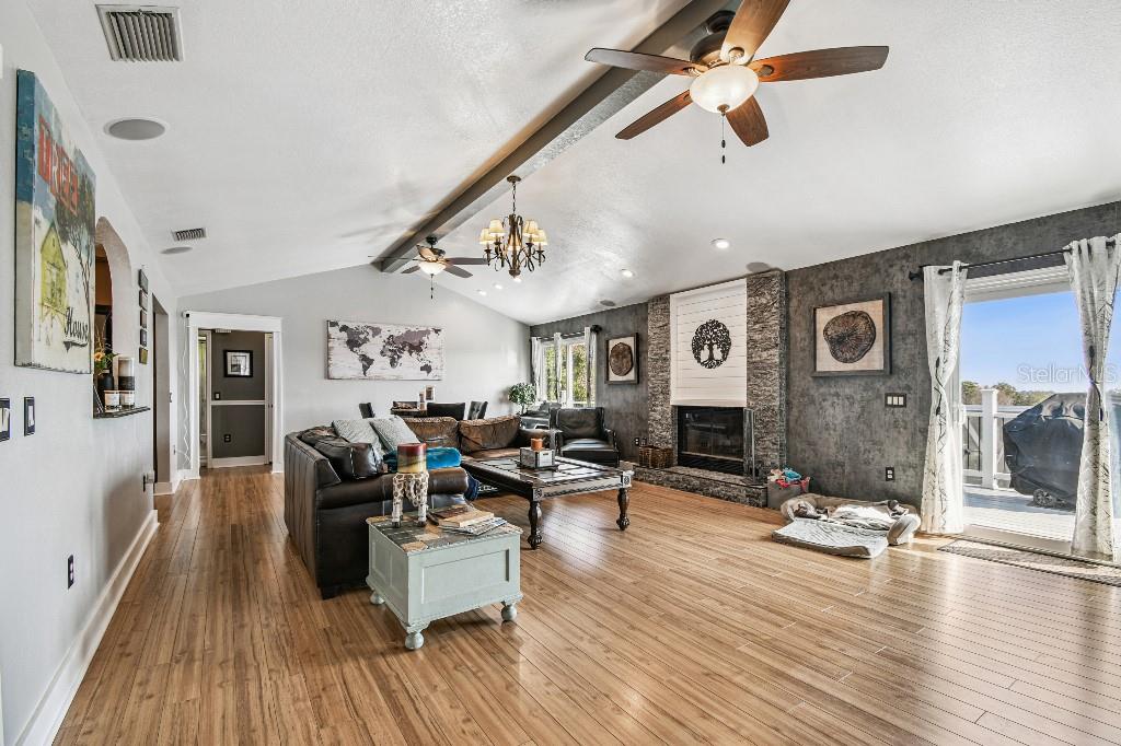 A living room features wood-look flooring, a stone fireplace, and a vaulted ceiling with fans — 6408 RUNNING BEAR DRIVE, LAKELAND, FL