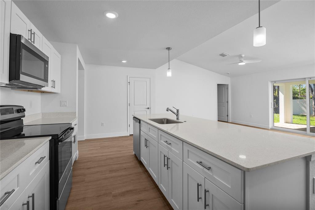 A modern kitchen features white cabinetry, quartz countertops, a center island, and wood-look flooring — 23377 AVACADO AVENUE, PORT CHARLOTTE, FL