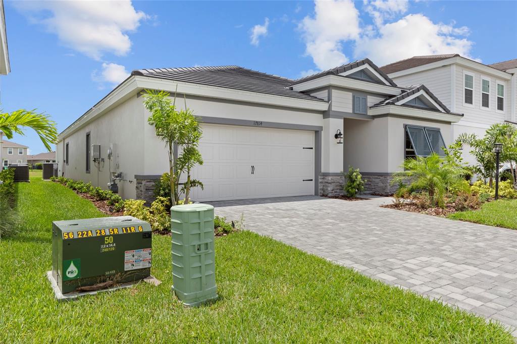 A single-story house with a paved driveway, two-car garage, and a green utility box nearby — 17814 CROPSIDE TRAIL, BRADENTON, FL